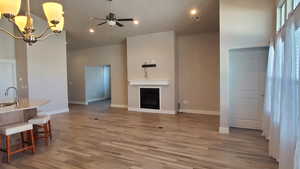 Living area featuring a ceiling fan, a high ceiling, light wood finished floors, suspended lighting, and a fireplace