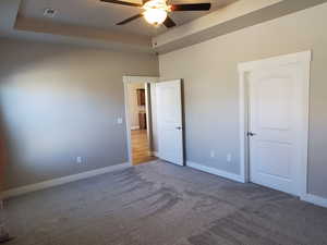 Unfurnished bedroom featuring a raised ceiling, dark carpet, and a ceiling fan