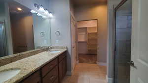 Bathroom featuring double vanity, a spacious closet, a stall shower, and light tile patterned floors