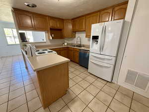 Kitchen with wood finish cabinetry, light countertops, white appliances, light tile patterned floors, and a textured ceiling