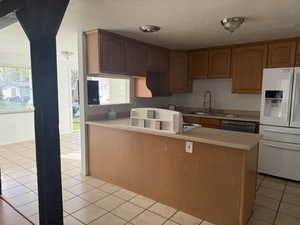 Kitchen featuring white refrigerator with ice dispenser, light countertops, wood finish cabinets, and stainless steel dishwasher