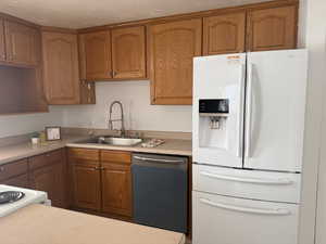 Kitchen with white refrigerator with ice dispenser, stainless steel dishwasher, wood finish cabinets, and light countertops