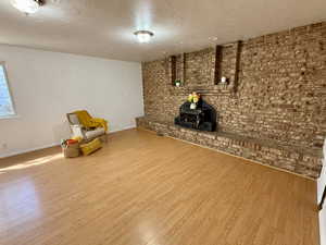 Unfurnished room featuring a textured ceiling, brick wall, wood finished floors, and a wood stove