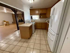 Kitchen with a peninsula, light countertops, white appliances, wood finish cabinetry, and light tile patterned floors