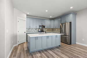 Kitchen with stainless steel appliances, gray cabinets, decorative backsplash, a center island with sink, and light wood-type flooring