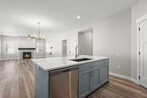 Kitchen featuring a fireplace, stainless steel dishwasher, a kitchen island with sink, dark wood-style flooring, and open floor plan
