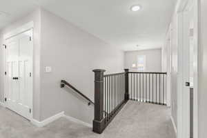 Corridor with light colored carpet, an upstairs landing, and hanging lights