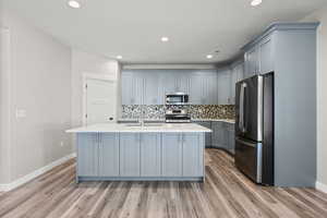 Kitchen featuring stainless steel appliances, gray cabinets, backsplash, a kitchen island with sink, and light stone counters
