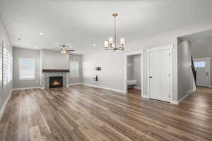Unfurnished living room with plenty of natural light, a tiled fireplace, ceiling fan, and a chandelier