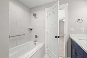 Full bathroom with vanity, tiled shower / bath combo, ceiling fan, and light tile patterned flooring