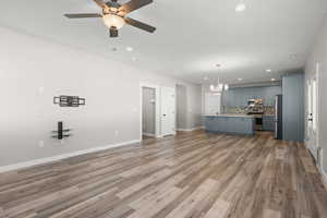 Unfurnished living room featuring a ceiling fan, dark wood-style flooring, and suspended lighting