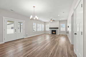Unfurnished living room with a fireplace, suspended lighting, light wood-type flooring, ceiling fan, and french doors