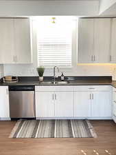 Kitchen featuring stainless steel dishwasher, dark wood-style flooring, and white cabinetry