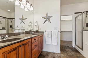 Bathroom featuring a shower stall, double vanity, a walk in closet, and dark stone finish flooring