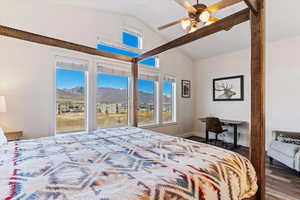 Bedroom featuring a mountain view, multiple windows, vaulted ceiling, dark wood-style floors, and a ceiling fan
