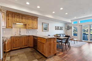 Kitchen with light stone countertops, a peninsula, wood finish cabinetry, decorative backsplash, and crown molding