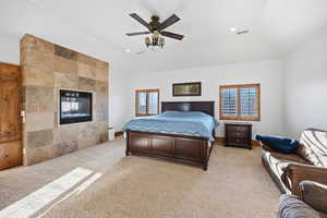 Bedroom with light colored carpet, recessed lighting, a ceiling fan, a tiled fireplace, and vaulted ceiling