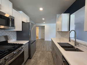 Dual tone kitchen featuring stainless steel appliances, recessed lighting, light stone countertops, two tone cabinetry, and decorative backsplash