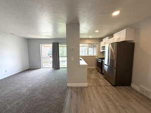Kitchen featuring stainless steel appliances, white cabinetry, light countertops, a textured ceiling, and light wood-type flooring
