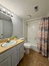 Full bathroom featuring a textured wall, vanity, a textured ceiling, shower / bath combo, and light tile patterned flooring