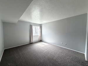 Carpeted spare room featuring a textured ceiling and baseboards
