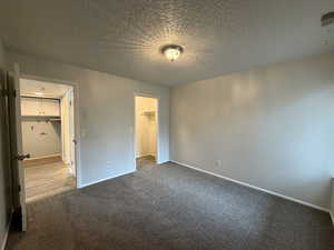 Unfurnished bedroom with a spacious closet, carpet flooring, and a textured ceiling