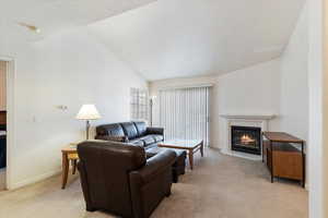 Living room with lofted ceiling, a glass covered fireplace, and light colored carpet