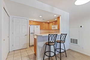 Kitchen with light countertops, white appliances, a kitchen bar, a peninsula, and recessed lighting