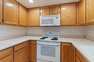 Kitchen with white appliances, light countertops, and wood finish cabinetry