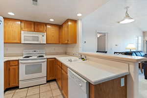Kitchen featuring white appliances, light countertops, wood finish cabinetry, a peninsula, and light tile patterned floors