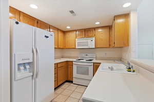 Kitchen with white appliances, light countertops, recessed lighting, light tile patterned flooring, and wood finish cabinets