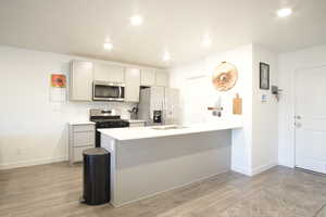 Kitchen featuring a peninsula, light wood-style floors, stainless steel appliances, gray cabinets, and recessed lighting