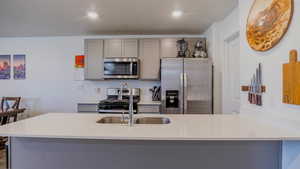Kitchen with gray cabinetry, stainless steel appliances, a peninsula, light stone countertops, and recessed lighting