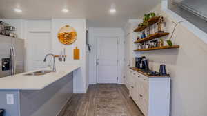 Kitchen featuring a peninsula, stainless steel refrigerator with ice dispenser, white cabinetry, dark wood-style floors, and light stone countertops