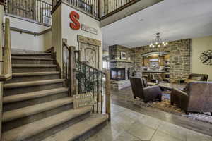 Stairs with a high ceiling, a stone fireplace, a chandelier, and wood finished floors
