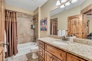 Ensuite bathroom with vanity, a textured ceiling, shower / bath combination with curtain, and light tile patterned floors
