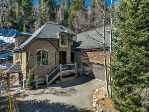 View of front facade featuring stone siding, a shingled roof, driveway, and a garage