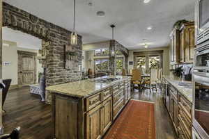 Kitchen with a kitchen island, wood finish cabinets, dark wood-style flooring, light stone countertops, and a textured ceiling