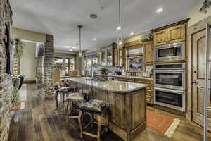 Kitchen featuring wood finish cabinetry, stainless steel appliances, a kitchen breakfast bar, light stone counters, and decorative light fixtures