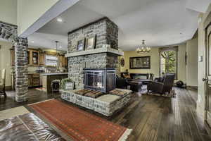 Living area with dark wood-style floors, a chandelier, a fireplace, decorative columns, and a textured ceiling
