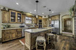 Kitchen featuring stainless steel appliances, wood finish cabinets, pendant lighting, a center island, and light stone countertops