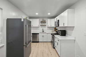 Kitchen with stainless steel appliances, open shelves, white cabinets, light wood-style floors, and recessed lighting