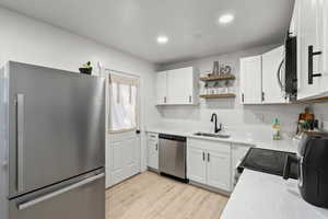 Kitchen featuring stainless steel appliances, open shelves, white cabinetry, light wood-style flooring, and recessed lighting