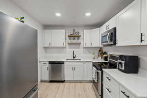 Kitchen featuring stainless steel appliances, open shelves, white cabinetry, light wood finished floors, and light stone counters