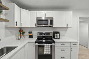 Kitchen featuring stainless steel appliances, open shelves, white cabinetry, light stone countertops, and light wood-style flooring