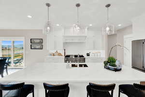 Kitchen with a breakfast bar area, a large island, light stone counters, and white cabinetry