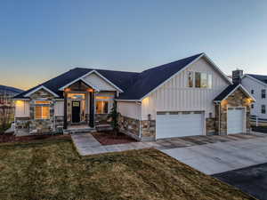 View of front of house featuring stone siding, board and batten siding, concrete driveway, a front lawn, and a garage