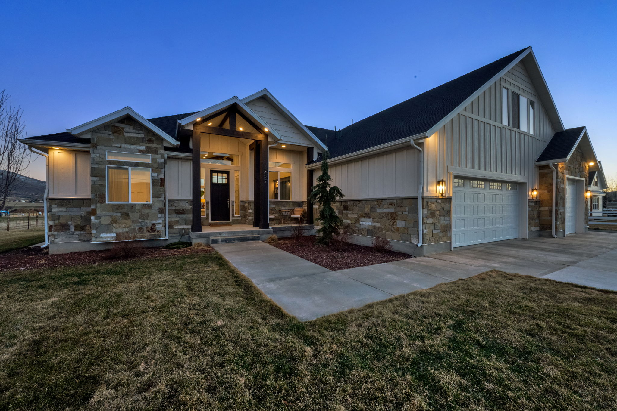 Modern inspired farmhouse with board and batten siding, stone siding, a front yard, and concrete driveway