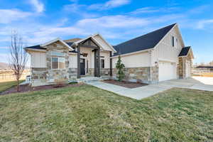 Modern farmhouse with stone siding, board and batten siding, a front yard, and concrete driveway