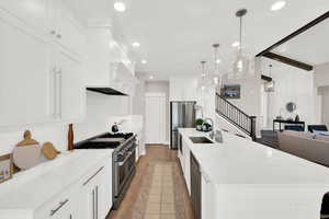 Kitchen featuring beam ceiling, light wood finished floors, stainless steel appliances, open floor plan, and a large island with sink